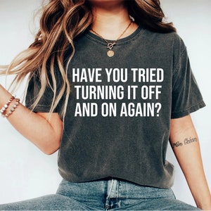 May include: A dark gray t-shirt with the text "HAVE YOU TRIED TURNING IT OFF AND ON AGAIN?" printed in white.