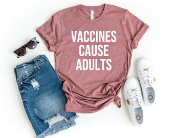 Puede incluir: Una camiseta color malva con el texto "Vaccines Cause Adults" impreso en blanco. La camiseta se combina con pantalones cortos de mezclilla y zapatillas blancas.