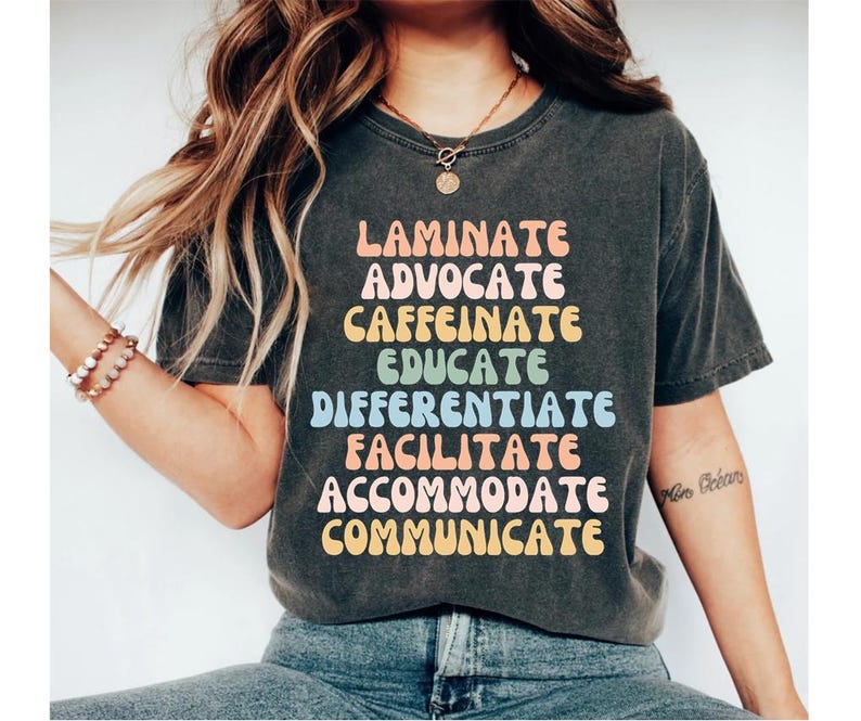 Puede incluir: Una camiseta gris oscura con un dise&ntilde;o gr&aacute;fico colorido que dice "Laminate, Advocate, Caffeinate, Educate, Differentiate, Facilitate, Accommodate, Communicate".