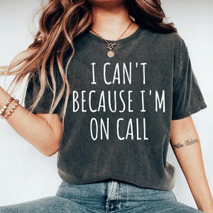 May include: A dark gray t-shirt with the text "I can't because I'm on call" printed in white.