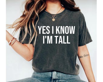 May include: A dark gray t-shirt with the text "YES I KNOW I'M TALL" printed in white.