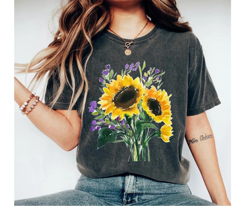 May include: A dark gray t-shirt with a floral design featuring three yellow sunflowers with purple flowers and green leaves.