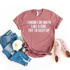 May include: A mauve t-shirt with the text "I know I do math like a girl try to keep up" printed in white.