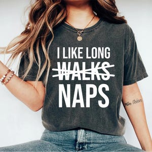 May include: A dark gray t-shirt with the text "I like long walks" crossed out and "naps" written below it.