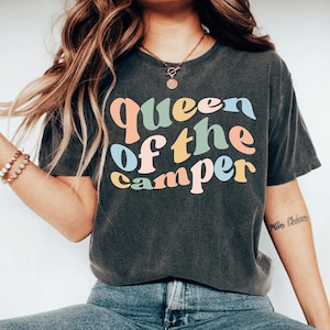 May include: A dark grey t-shirt with the text "Queen of the Camper" in colorful, retro-style lettering.