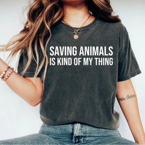 May include: A dark gray t-shirt with the text "SAVING ANIMALS IS KIND OF MY THING" printed in white on the front.