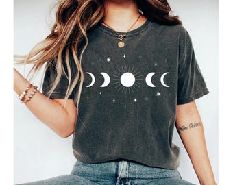 May include: A dark gray t-shirt with a white moon and sun graphic. The graphic features a sun with rays and three crescent moons. The shirt has a distressed look.