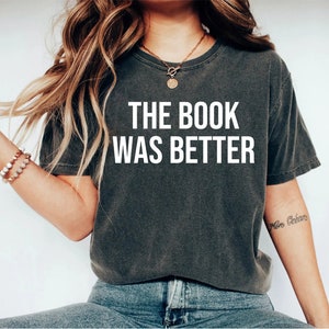 May include: A dark gray t-shirt with the text "THE BOOK WAS BETTER" printed in white on the front.