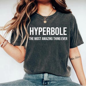 May include: A dark gray t-shirt with the text "HYPERBOLE THE MOST AMAZING THING EVER" printed in white.