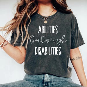 May include: A dark gray t-shirt with the text "Abilities Outweigh Disabilities" printed in white.