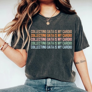 May include: A dark gray t-shirt with the text "COLLECTING DATA IS MY CARDIO" repeated five times in different colors. The text is in a rainbow color scheme.