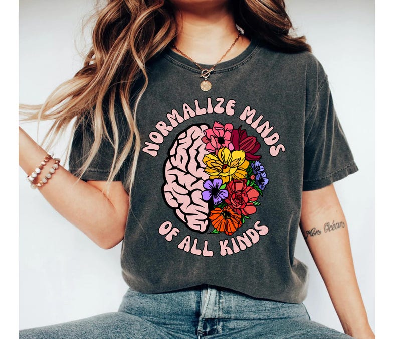 May include: A dark gray t-shirt with a pink brain graphic and flowers. The text "Normalize Minds of All Kinds" is printed on the shirt.