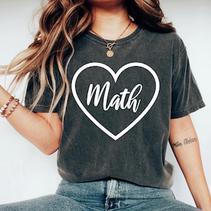 May include: A dark gray t-shirt with a white heart design that says "Math" inside. The shirt is worn by a person with long brown hair.