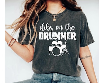 May include: A dark gray t-shirt with the text "dibs on the drummer" in white, featuring a white graphic of a drum set.