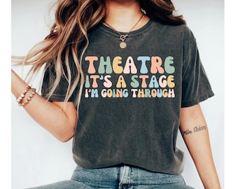 May include: A dark gray t-shirt with a colorful graphic that reads "Theatre It's a Stage I'm Going Through".