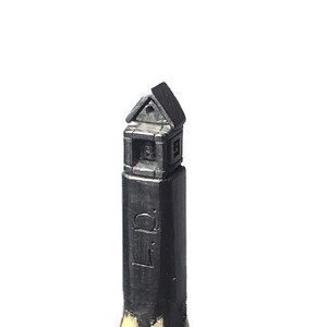 以下が含まれることがあります： 上部に小さな家の詳細な彫刻が施された黒い鉛筆。鉛筆は木製の表面に直立して立っています。