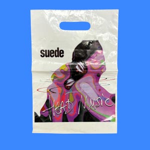 May include: A white plastic shopping bag with a die-cut handle. The bag features the black text "suede" and "HEAD MUSIC" in a stylised script font, overlaid on a colourful, abstract graphic design with swirling purple, pink, and green liquid patterns.