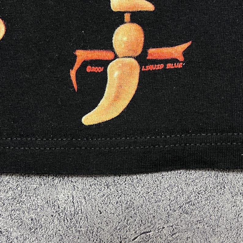 May include: Black t-shirt with a graphic design featuring a stylized orange chili pepper shape. The text "LIQUID BLUE" and "&copy;2001" are also visible in orange. The design is centered on the shirt.