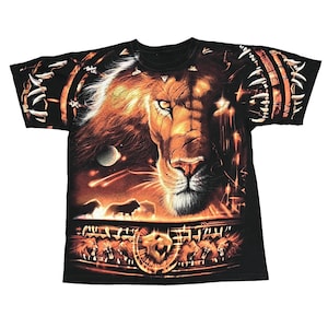 May include: Black t-shirt featuring a detailed graphic of a lion's face with a fiery mane and glowing eyes. The design includes a night sky with planets and shooting stars, and a border of lion heads.