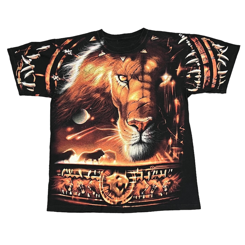 May include: Black t-shirt featuring a detailed graphic of a lion's face with a fiery mane and glowing eyes. The design includes a night sky with planets and shooting stars, and a border of lion heads.