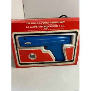 Könnte beinhalten: Ein blaues RAC D.C. Power Timing Light in der originalen roten Box. Die Box hat weiße und schwarze Verzierungen und Text in Englisch und Französisch. Das Timing Light hat die Form einer Pistole.
