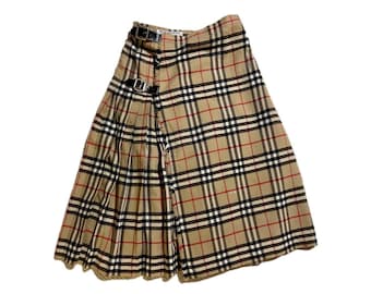 May include: A beige plaid kilt with black, red, and white lines. The kilt has a pleated design and two black leather buckle closures. The kilt is made of a woven fabric.