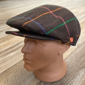 May include: A brown tweed newsboy cap with a plaid pattern in orange, green, and blue. The cap has a button on the side.