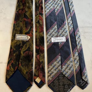 Puede incluir: Cuatro corbatas de seda con varios diseños. Dos corbatas presentan diseños florales en verde oliva, negro y rojo. Las otras dos tienen diseños de rayas en azul marino, rosa y blanco. Cada corbata tiene una etiqueta de marca.