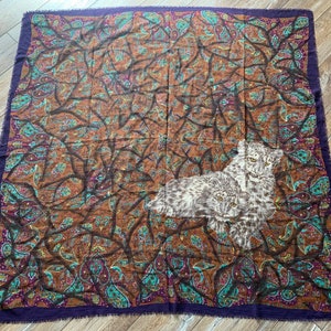 May include: A brown and purple paisley patterned scarf with a white and gray image of two snow leopards.