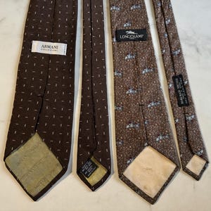 May include: Four brown neckties with different patterns. One tie has a dotted design with an "ARMANI COLLEZIONI" label. Another has a similar dotted pattern. The third tie has a floral pattern with a "LONGCHAMP" label. The fourth tie has a small pattern.