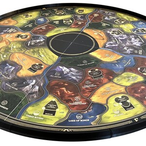 Può includere: Un tabellone da gioco circolare con un bordo esterno nero e un bordo interno dorato. Il tabellone è diviso in sezioni con colori e disegni diversi, tra cui montagne, fiumi e foreste. Il tabellone è fatto di cartone ed è progettato per essere utilizzato con un gioco da tavolo.