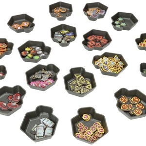 Peut inclure: Un ensemble de 15 plateaux hexagonaux en plastique contenant des pièces de jeu de différentes couleurs. Les plateaux sont gris et les pièces sont rouges, jaunes, vertes, bleues et orange.