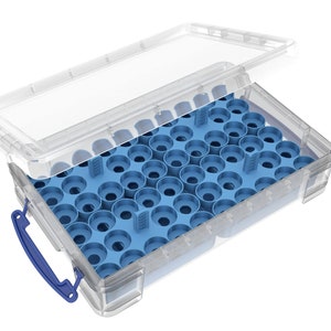 Può includere: Una scatola di plastica trasparente con un inserto interno blu. L'inserto ha più scomparti circolari. La scatola ha una maniglia blu e un coperchio trasparente parzialmente aperto.