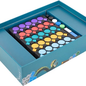 Può includere: Una scatola da gioco blu turchese con un inserto in schiuma per riporre i pezzi del gioco. L'inserto ha scomparti per diversi pezzi colorati, tra cui rosso, arancione, giallo, verde, blu e viola. La scatola ha un design a drago sul fondo.