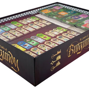 May include: The Castles of Burgundy board game box is open, revealing the game components, including tiles, meeples, and cards. The box is black with gold lettering that reads "The Castles of Burgundy".