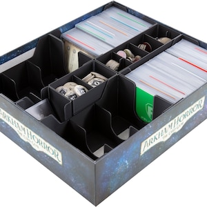 Pode incluir: Um organizador de jogos de cartas preto com vários compartimentos, preenchido com cartas, fichas e peças de jogo. A caixa tem um design de noite estrelada e o texto "ARKHAM HORROR THE CARD GAME".