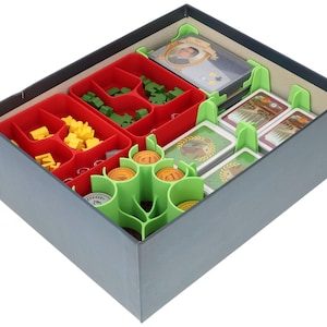 Könnte beinhalten: Ein grüner und roter Organizer-Einsatz für eine Brettspielbox. Der Einsatz hat Fächer für Karten, Spielsteine und andere Spielteile. Der Einsatz ist aus Kunststoff und hat ein grün-rotes Farbschema.