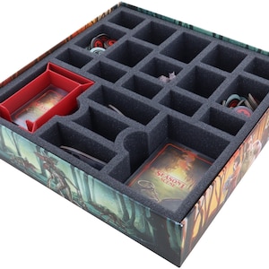 Könnte beinhalten: Ein Schaumstoffeinsatz für eine Brettspielbox mit Fächern zum Verstauen von Spielfiguren, Karten und anderem Zubehör. Der Einsatz ist grau und hat einen roten Teiler. Der Einsatz befindet sich in einer Box mit einer Waldszene auf der Außenseite.