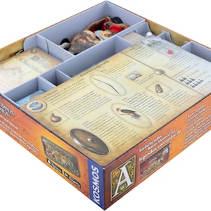 Könnte beinhalten: Eine Spielbox mit Fächern, die Spielsteine und Karten enthalten. Die Box trägt den Spieltitel "GEHEIMNIS KONIGS" und das Kosmos-Logo. Die Box ist in Abschnitte zur Organisation unterteilt, wobei Karten und Spielsteine sichtbar sind.