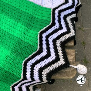 May include: A green, black, white, and gray crocheted blanket with a zig-zag pattern. The blanket has a fringe border and is made with a variety of yarn textures.