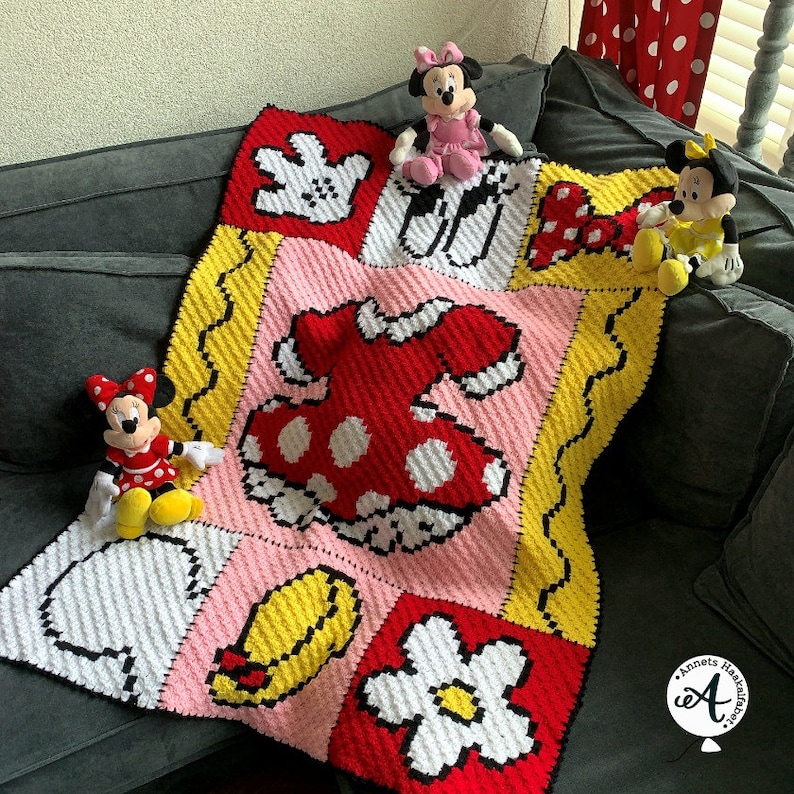 Peut inclure: Une couverture au crochet sur le th&egrave;me de Mickey Mouse. La couverture est compos&eacute;e de carr&eacute;s color&eacute;s avec des images des gants de Mickey Mouse, une robe, une fleur et un chapeau. Il y a trois peluches Mickey Mouse sur la couverture.