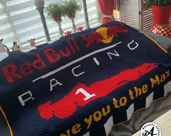 May include: A blue and red crocheted blanket with the words "Red Bull Racing" and "Love you to the Max" in white. The blanket features a red and yellow bull logo and a red race car with the number 1.