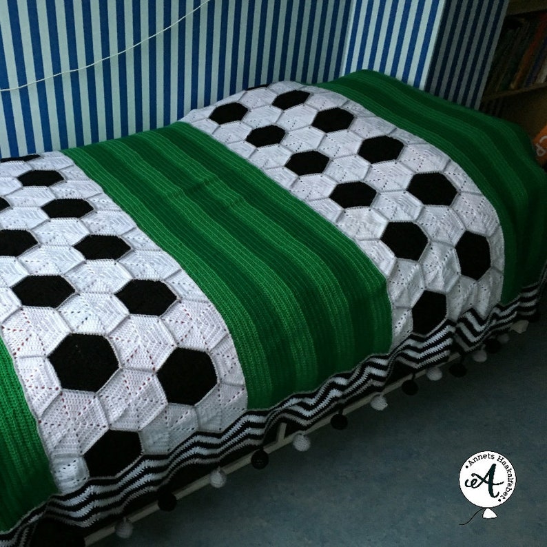May include: A green, white, and black crocheted blanket with a soccer ball design. The blanket has a black and white zigzag trim with white pom-poms.