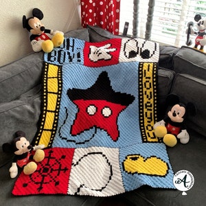 Könnte beinhalten: Eine blaue, gelbe, rote, weiße und schwarze gehäkelte Decke mit Mickey Mouse-Figuren, einem Stern und den Worten "Oh Boy!" Die Decke liegt auf einem grauen Sofa.