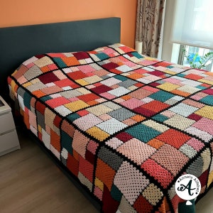 Könnte beinhalten: Eine bunte Häkeldecke mit geometrischem Muster in Rot-, Orange-, Gelb-, Grün-, Blau- und Grautönen. Die Decke ist aus schwarzem Garn gefertigt und hat einen weißen Rand. Die Decke liegt auf einem Bett mit einem dunklen Kopfteil.
