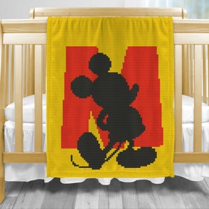 May include: A yellow and red crocheted baby blanket with a black silhouette of Mickey Mouse. The blanket features the letter "M" in red.