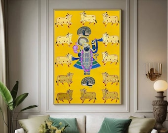 Può includere: Un dipinto colorato su sfondo giallo raffigura una divinità indù in piedi al centro circondata da 16 mucche. La divinità indossa un abito blu e oro con un copricapo di piume di pavone. Il dipinto è incorniciato e appeso a una parete in un soggiorno.
