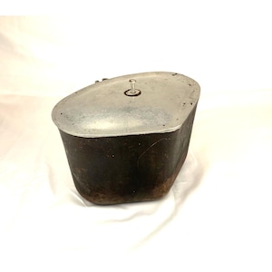 May include: A vintage metal container with a lid. The container is dark brown with a rectangular shape and rounded edges. The lid is silver-colored and has a small handle. The container is likely used for storage.