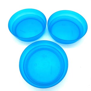 May include: Three round, translucent blue plastic bowls arranged in a triangular formation. Each bowl features a smooth, circular rim and a flat base, with a consistent vibrant blue color throughout the semi-transparent material of the set.