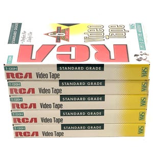 Könnte beinhalten: Ein Stapel von fünf RCA T-120H Standard-VHS-Videokassettenhüllen. Jede weiß-gelbe Hülle zeigt das rote RCA-Logo, den Text Video Tape und eine Grafik, die bis zu 6 Stunden Spielzeit anzeigt. Die Hüllen sind vertikal übereinander gestapelt.